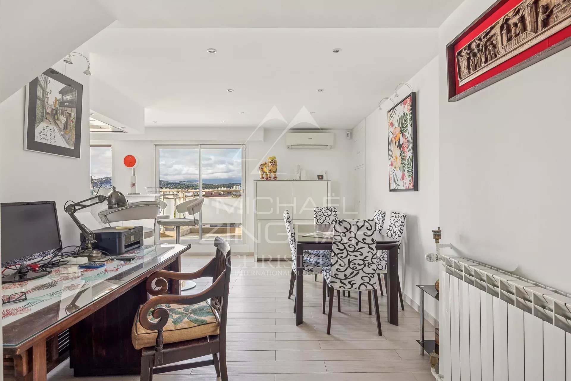 Intérieur d'un appartement moderne avec un bureau, des chaises élégantes et une vue sur la mer.
