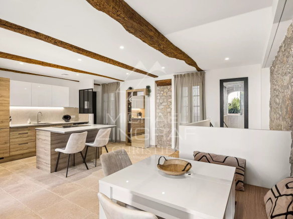 Intérieur d'un duplex moderne avec salon, cuisine et salle à manger, murs en pierre et poutres apparentes.