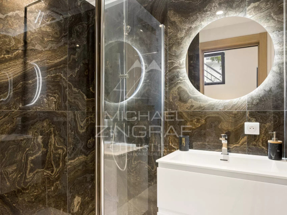 Salle de bain moderne avec douche, miroir rond et meuble lavabo en blanc.