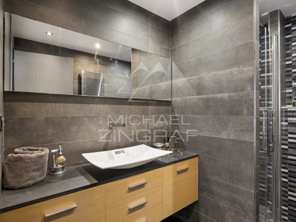 Salle de bain moderne avec meuble en bois et lavabo design, murs en carrelage gris.