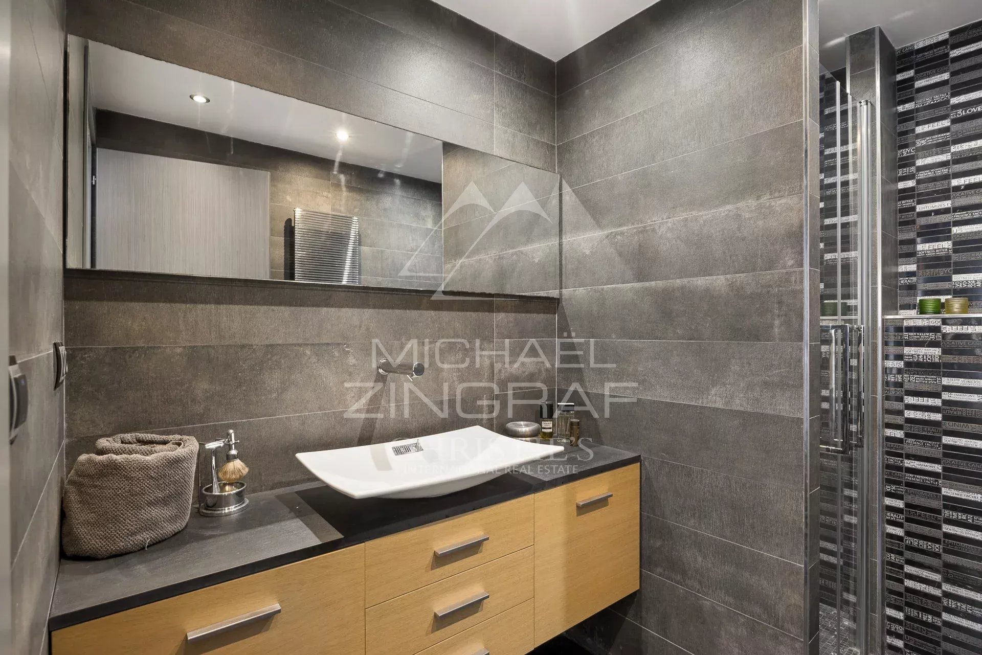 Salle de bain moderne avec meuble en bois et lavabo design, murs en carrelage gris.