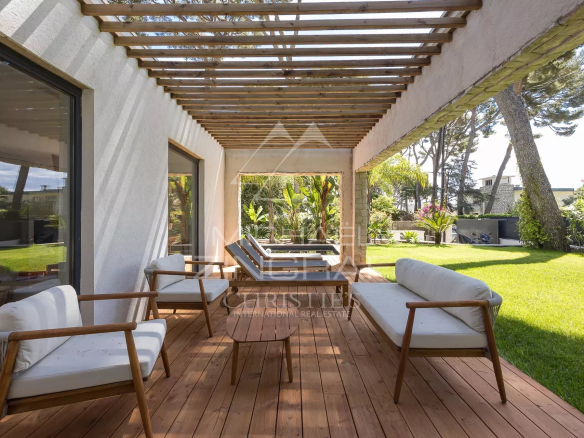 Terrasse d'une villa contemporaine avec mobilier en bois et jardin verdoyant au Cap d'Antibes.