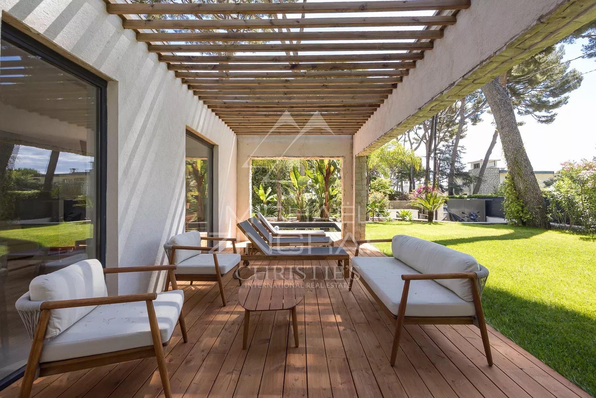 Terrasse de villa contemporaine au Cap d’Antibes Terrasse d'une villa contemporaine avec mobilier en bois et jardin verdoyant au Cap d'Antibes.