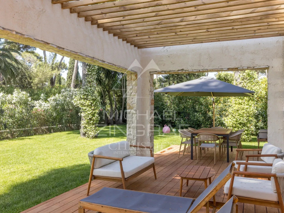 Terrasse d'une villa contemporaine avec mobilier en bois et parasol, entourée de verdure.