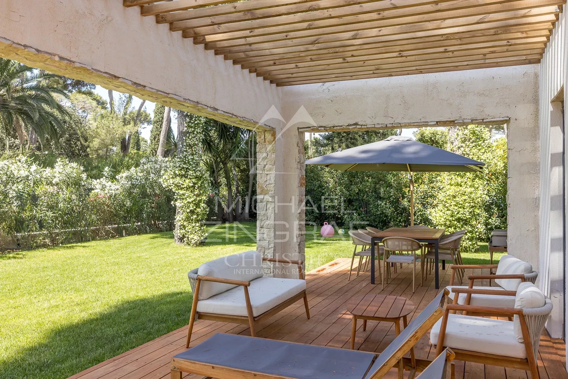 Terrasse d’une villa contemporaine au Cap d’Antibes Terrasse d'une villa contemporaine avec mobilier en bois et parasol, entourée de verdure.