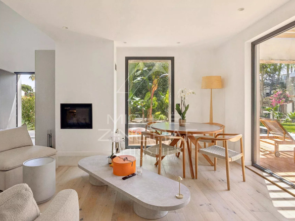 Intérieur d'une villa contemporaine avec salon lumineux et coin repas, fenêtres ouvertes sur terrasse.