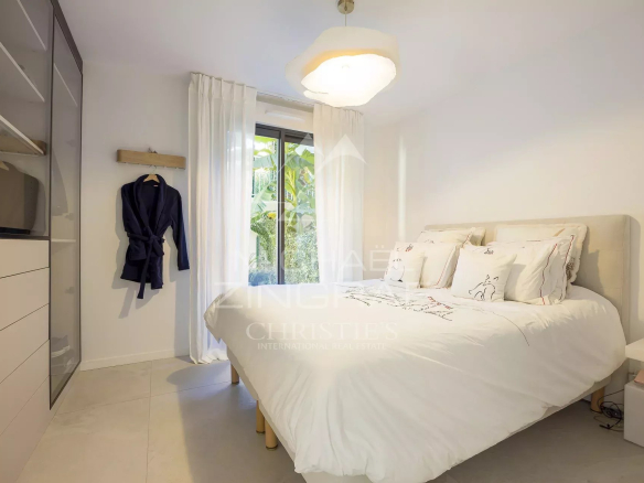 Chambre d'un appartement en rez-de-jardin à Antibes avec lit double et fenêtre donnant sur le jardin.