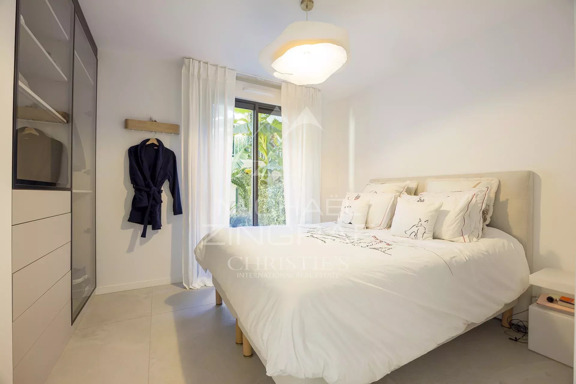 Chambre d'un appartement en rez-de-jardin à Antibes avec lit double et fenêtre donnant sur le jardin.