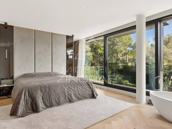 Chambre moderne avec lit, fenêtres larges et vue sur un jardin paysager.