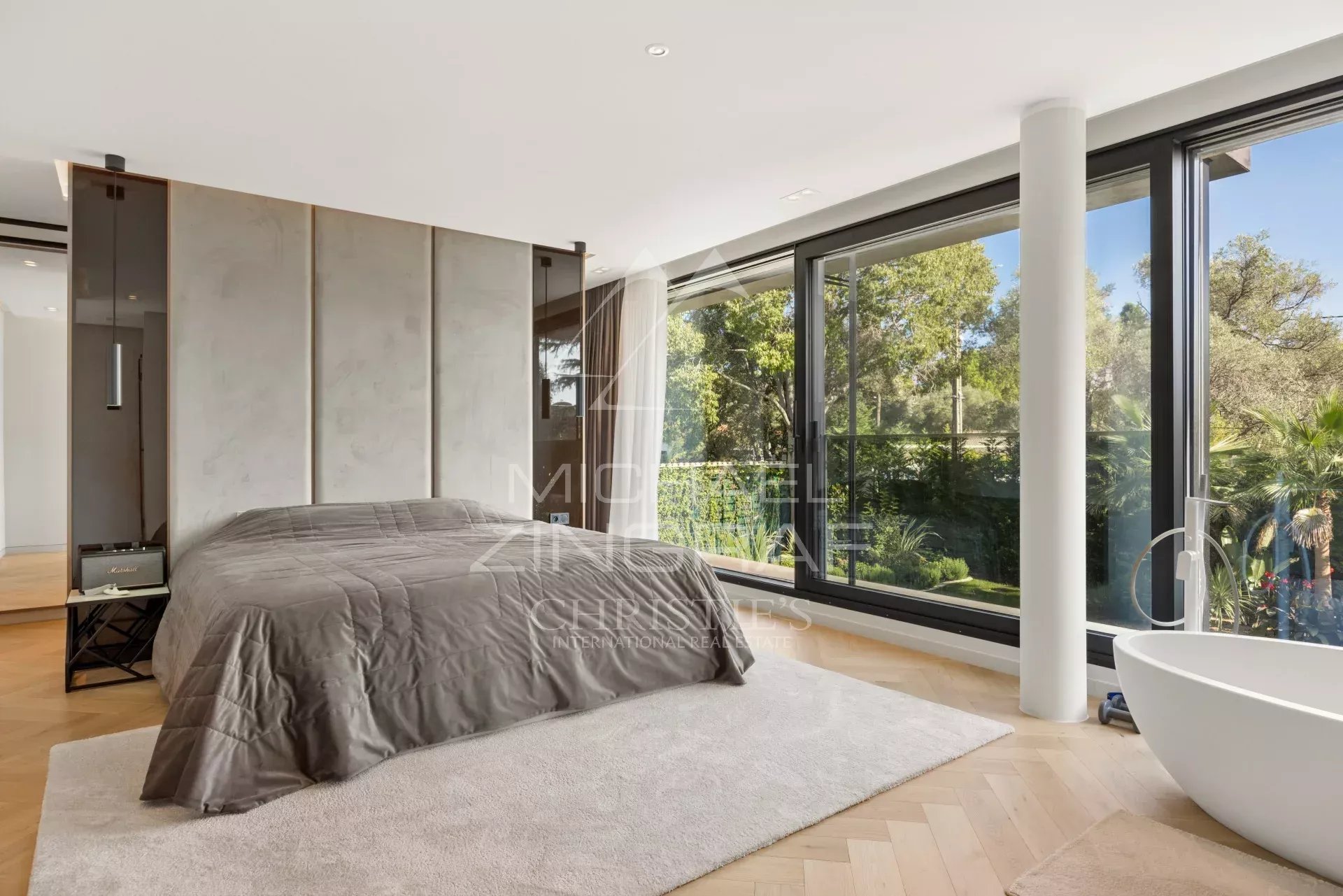 Chambre moderne avec lit, fenêtres larges et vue sur un jardin paysager.