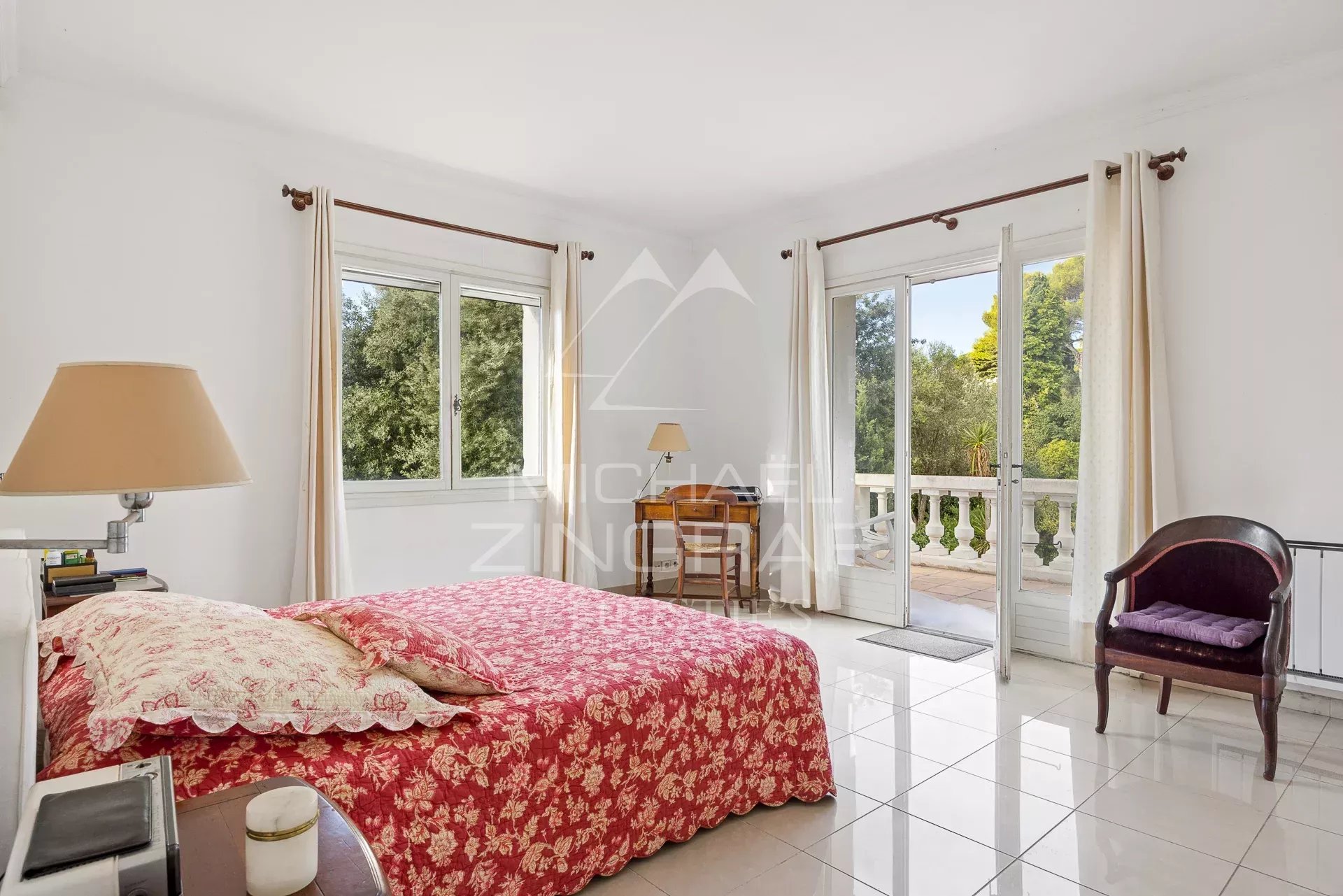 Bright room in Antibes Spacious room with bed and windows opening onto a balcony, decorated with flowers.
