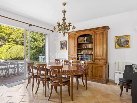 Dining room with wooden table and bookcase, natural light through the windows.