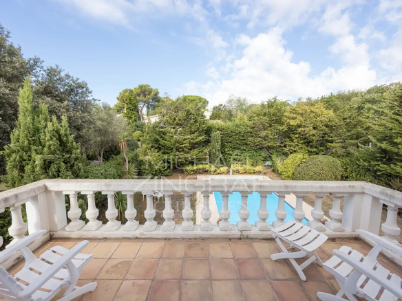 View from a balcony with white chairs, green garden and swimming pool in the background.