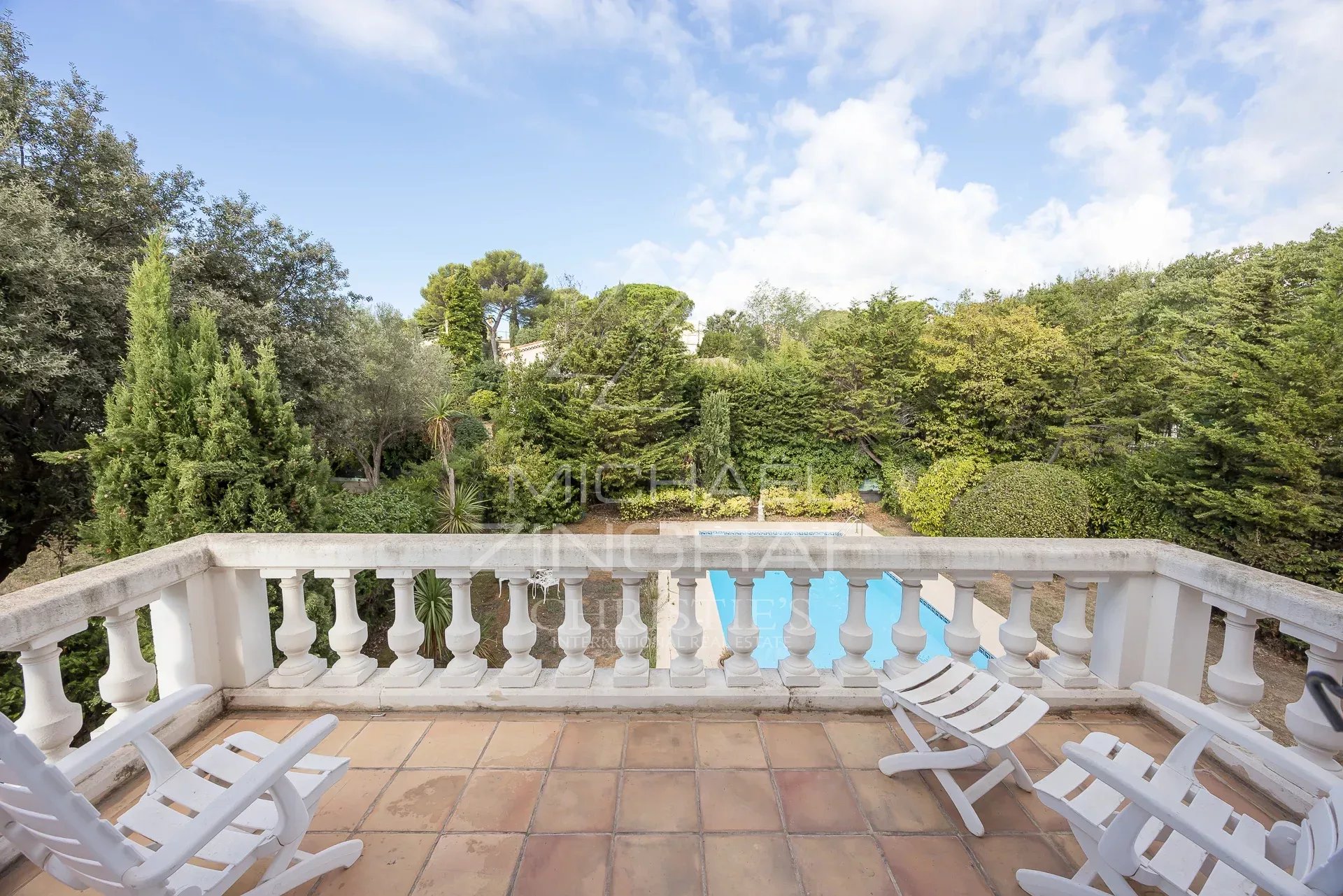 Balcony with views of the garden and pool View from a balcony with white chairs, green garden and swimming pool in the background.