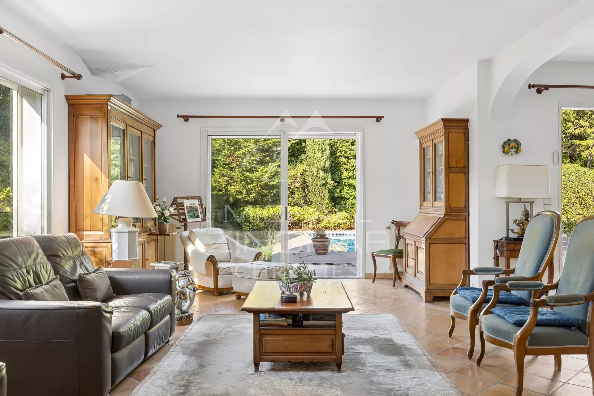 Property fair in Antibes Bright living room with views of the garden and pool, wooden furniture and comfortable sofas.