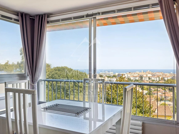 Vue depuis un appartement à Antibes avec une table et des chaises, offrant une vue panoramique sur la mer et la ville.