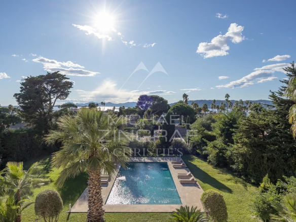 Vue d'une propriété avec piscine et jardins sur le versant ouest du Cap d'Antibes sous un ciel ensoleillé.