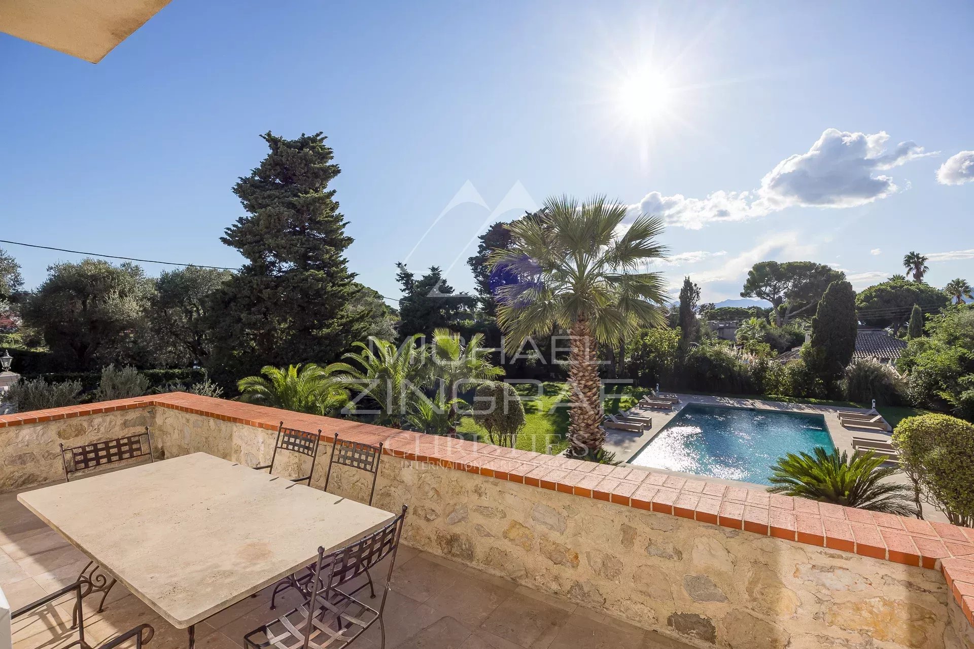 Vue sur la piscine et le jardin d'une villa moderne à Antibes sous un ciel ensoleillé.