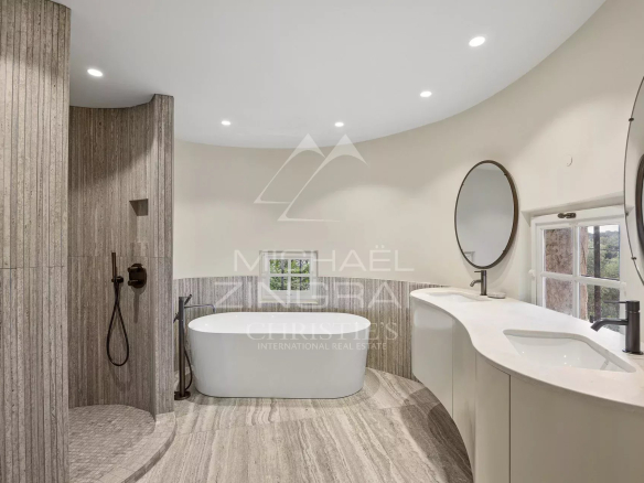 Salle de bains moderne avec baignoire et douche, murs en pierre, éclairage doux.