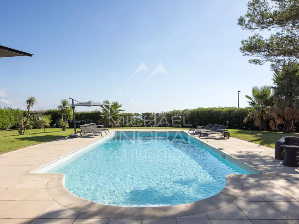 Piscine entourée de pelouse et de palmiers dans une villa au Cap d'Antibes.