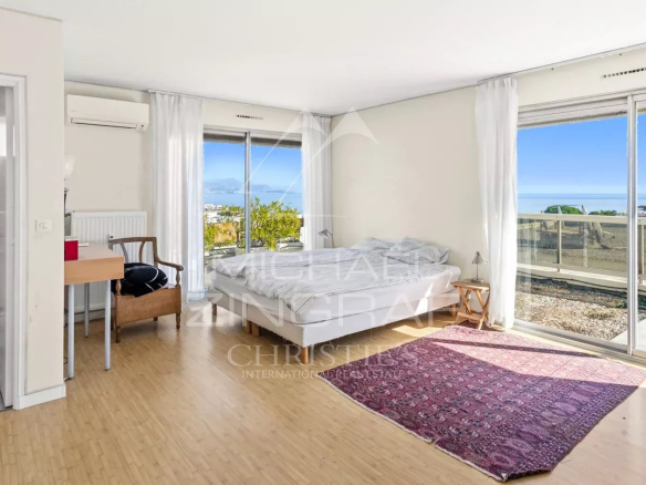 Intérieur d'une villa sur le toit avec vue mer, lit, bureau et accès à une terrasse.
