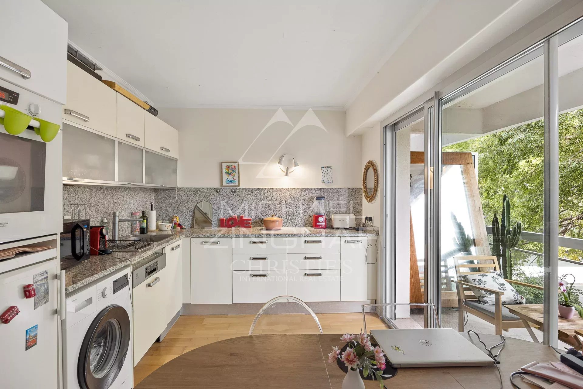 Cuisine moderne et lumineuse d'un appartement à Cap d'Antibes avec vue sur un parc arboré.
