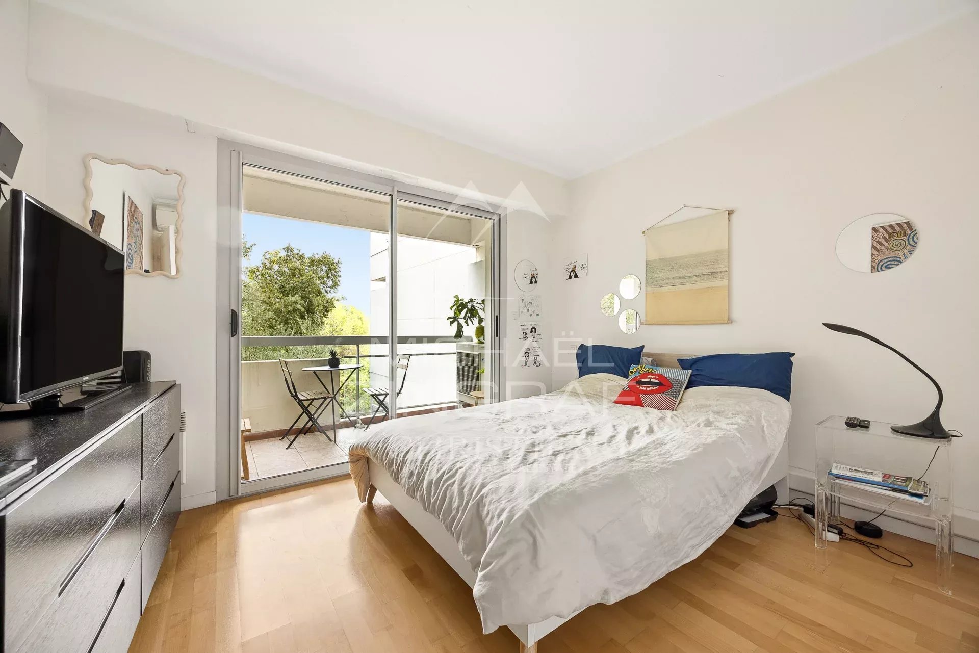 Chambre d'un appartement au Cap d'Antibes avec balcon et vue sur un parc arboré.