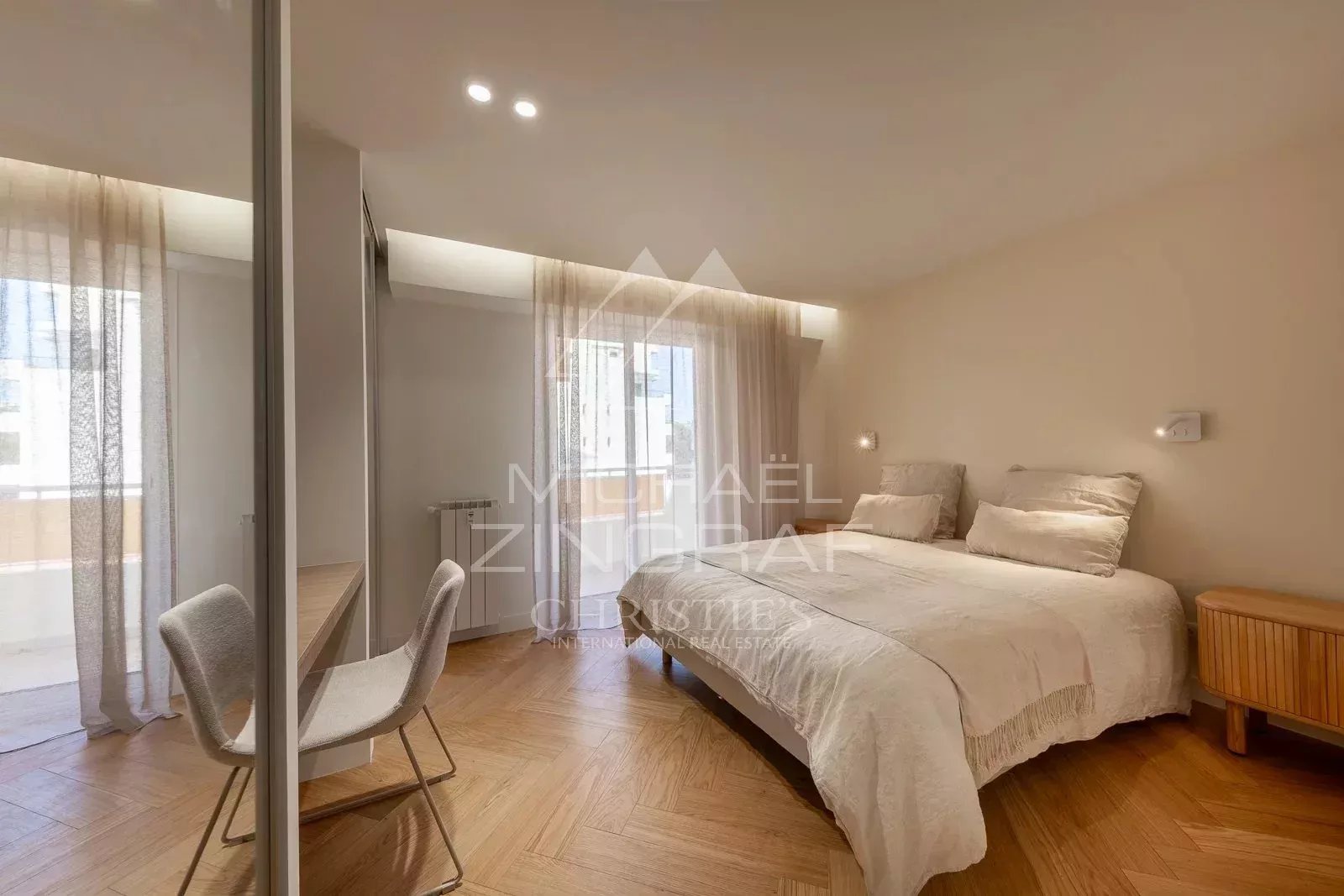 Bright room with double bed and desk, windows with light curtains.
