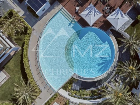 Vue aérienne de la piscine d'un complexe résidentiel à Antibes, entourée de palmiers et de chaises longues.