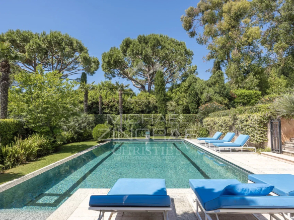 Swimming pool of a contemporary villa with sun loungers and lush garden in Cap d'Antibes.