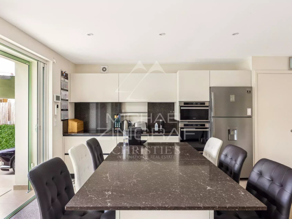 Cuisine moderne avec un grand îlot central et des chaises noires dans une maison rénovée à Antibes.