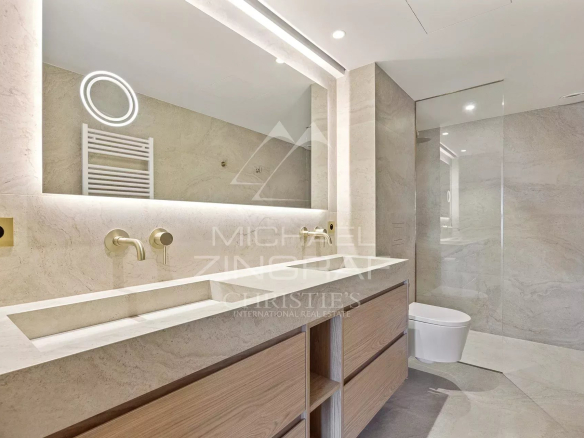 Contemporary bathroom with a double-sink vanity, light wood drawers, and a glass-walled shower in neutral marble tones.