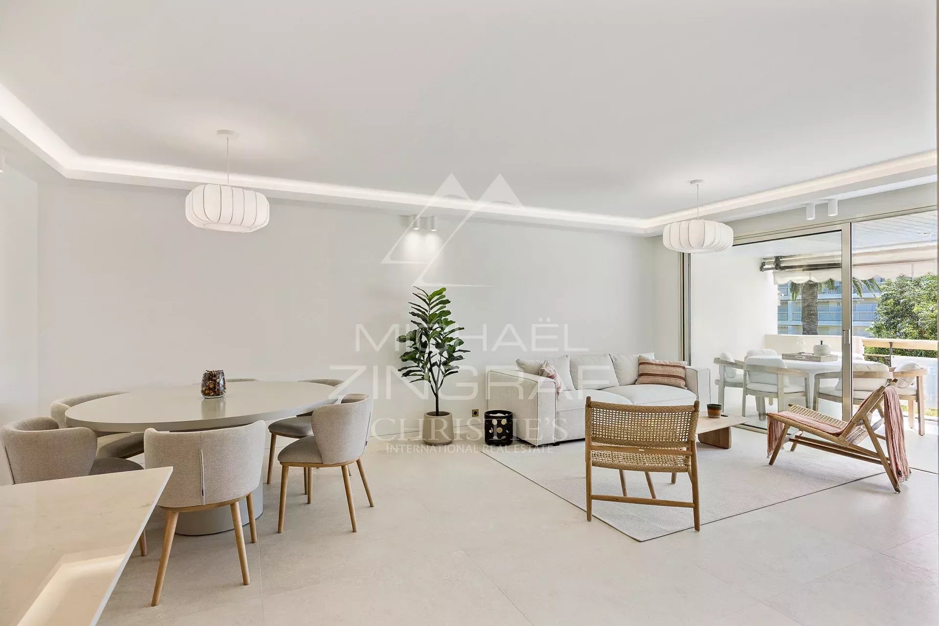 Bright open-concept living and dining space featuring a round dining table with beige chairs, a white sofa, wicker chair, and sliding glass doors to a balcony.