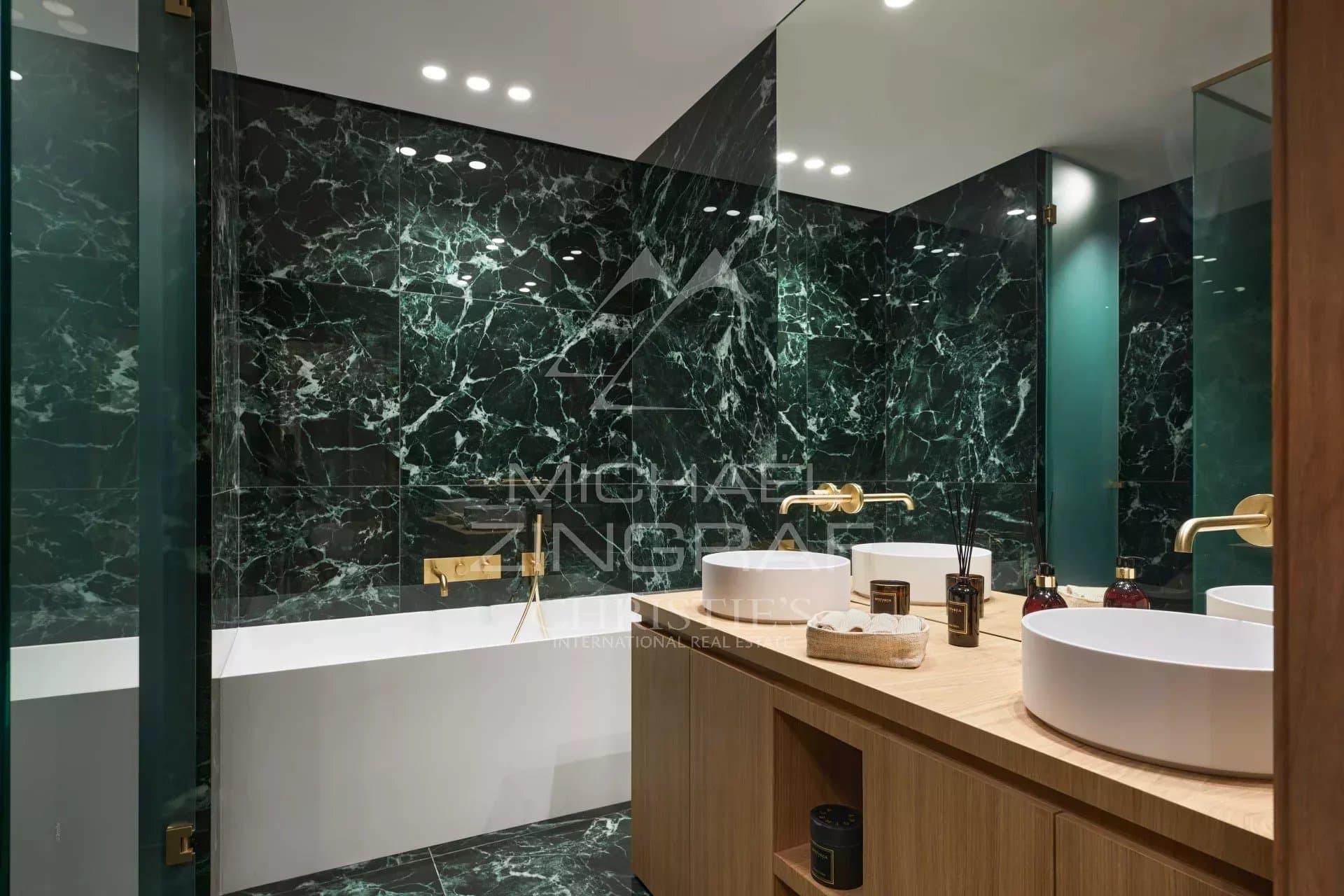 Salle de bain moderne avec baignoire et vasques, décorée de marbre vert et bois.