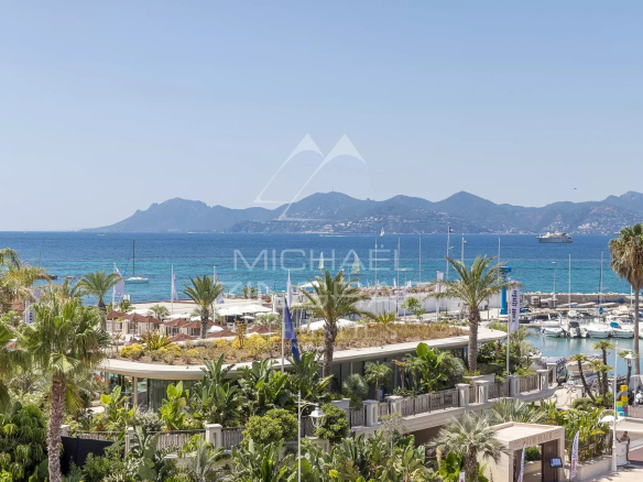 Vue sur la mer depuis une terrasse d'appartement à Cannes, avec palmiers et yachts au port.