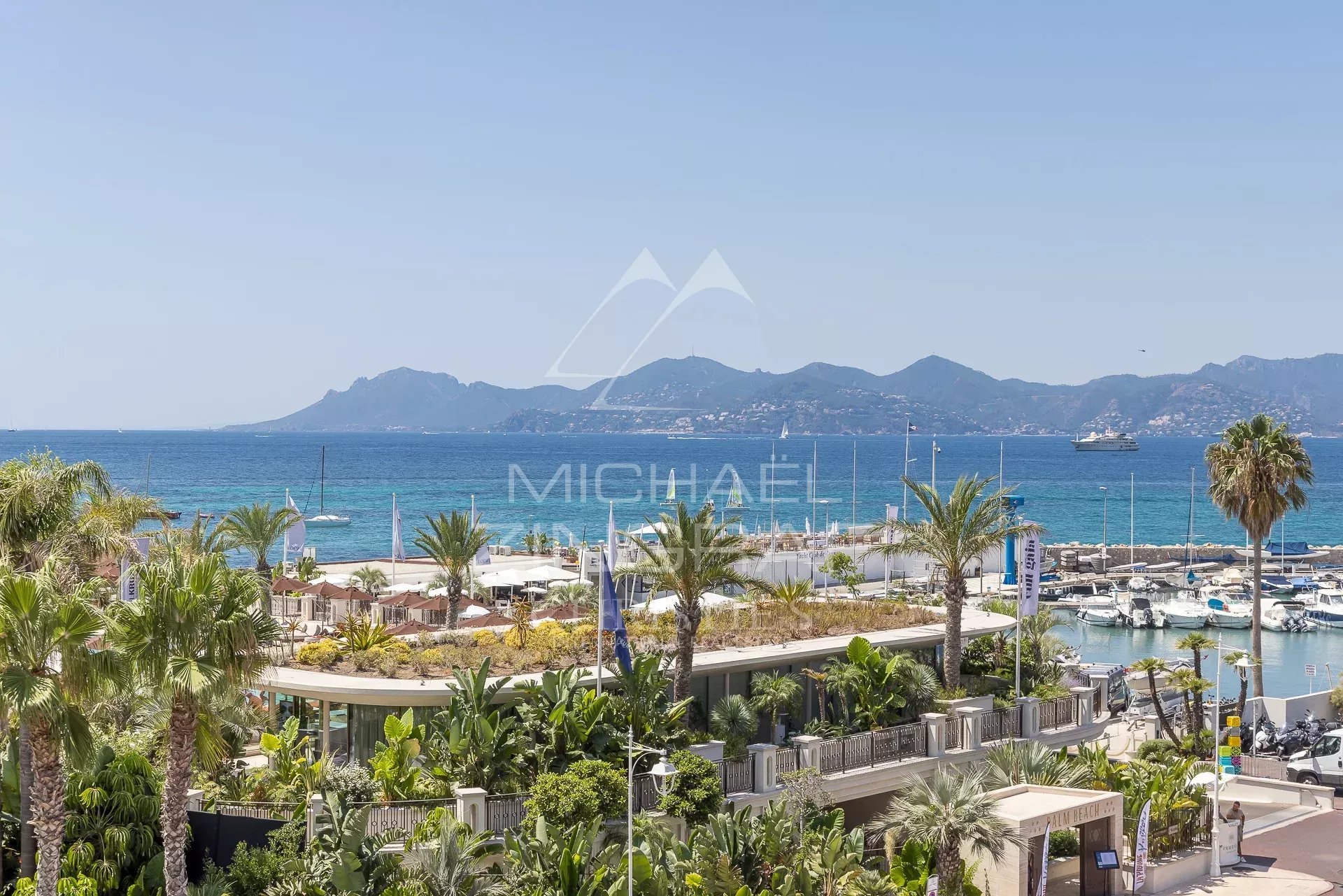Vue sur la mer depuis une terrasse d'appartement à Cannes, avec palmiers et yachts au port.