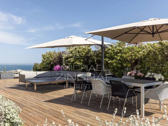 Terrace of a penthouse in Cannes with sea view, modern furniture and parasols.