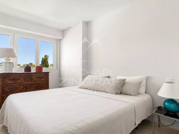 Chambre d'un appartement moderne à Cannes avec lit double et fenêtres lumineuses.