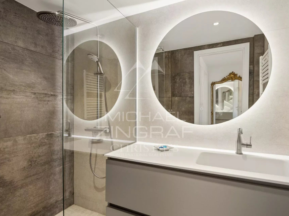 Salle de bain moderne avec douche et miroir rond, décorée en tons neutres