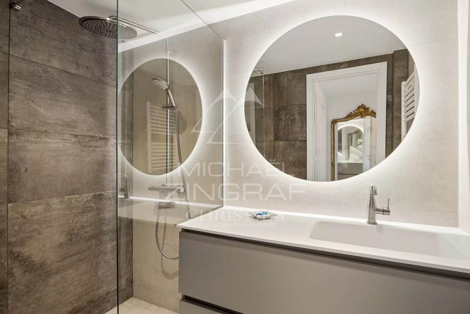 Salle de bain moderne avec douche et miroir rond, décorée en tons neutres