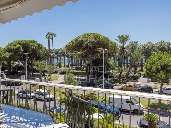 Vue depuis une terrasse d'un appartement à Cannes, avec des palmiers et la Croisette en arrière-plan.