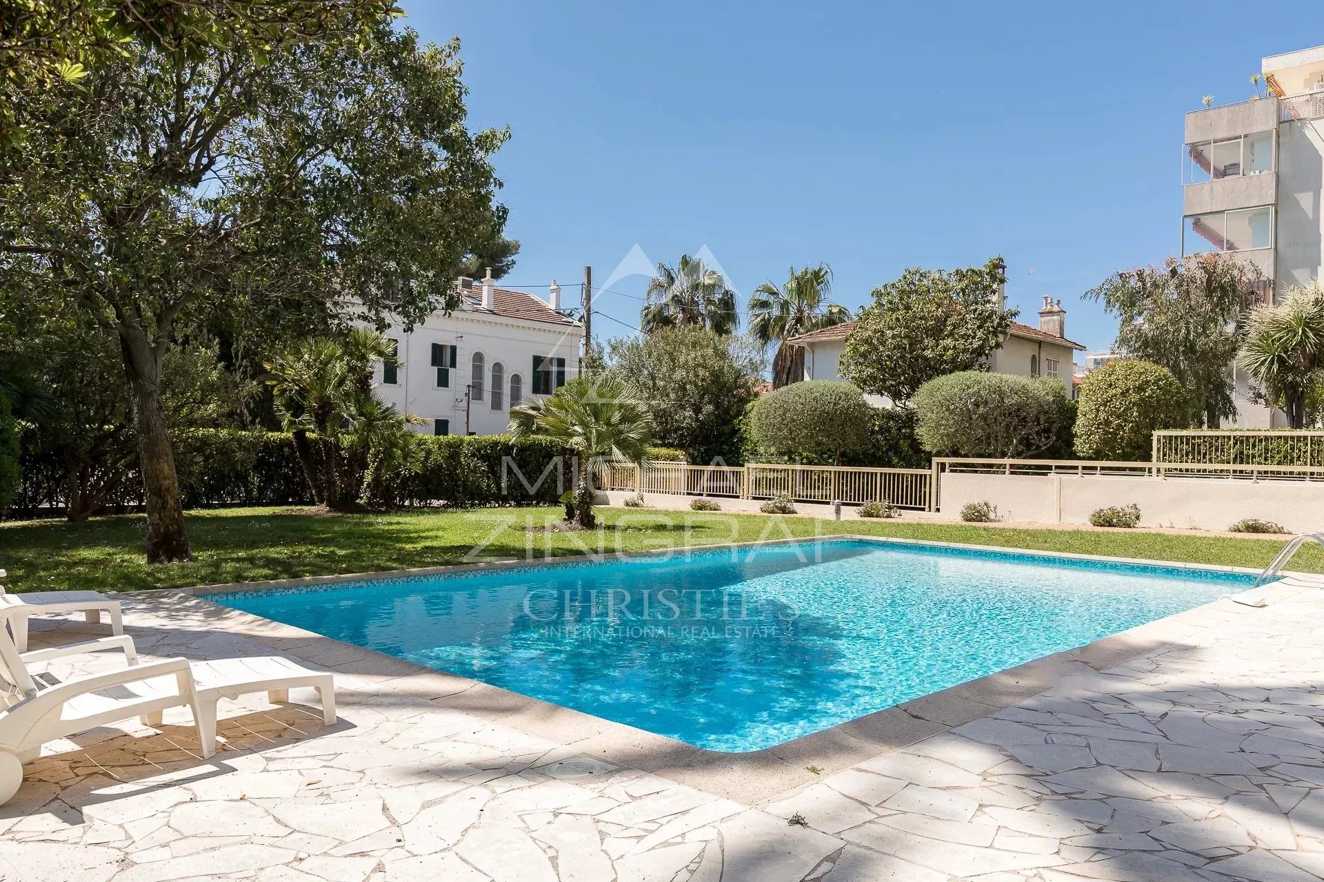 Swimming pool of a residence in Cannes Palm Beach, surrounded by trees and lawn.