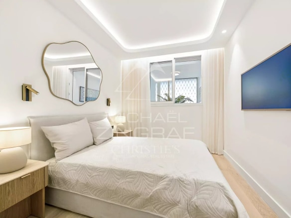 Chambre d'un appartement moderne avec lit, miroir et télévision murale.