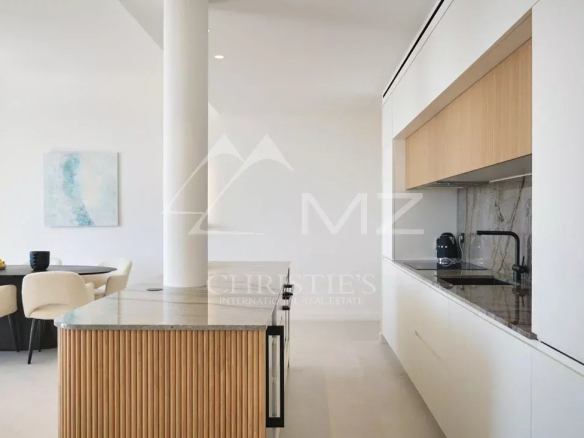 Cuisine moderne avec îlot arrondi et salon lumineux dans un appartement rénové à Cannes.
