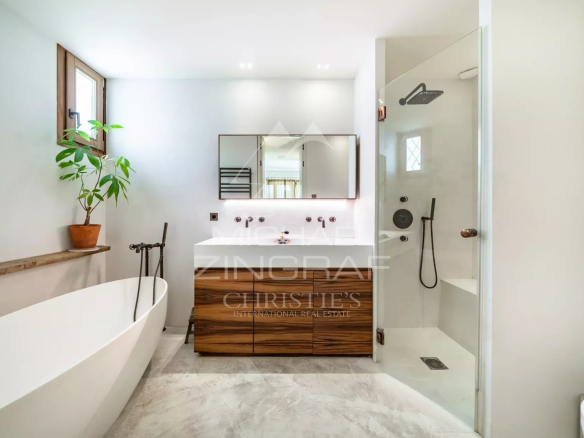 Salle de bain moderne avec baignoire et douche, plantes vertes, et meuble en bois.
