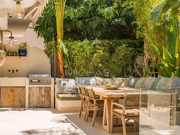 Terrasse avec mobilier en bois et cuisine extérieure, entourée de verdure, dans un appartement à Cannes.