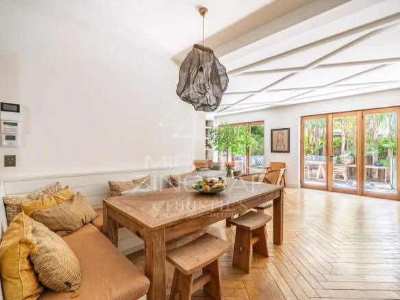 Intérieur d'un appartement à Cannes avec salle à manger en bois et accès à une terrasse tropicale.