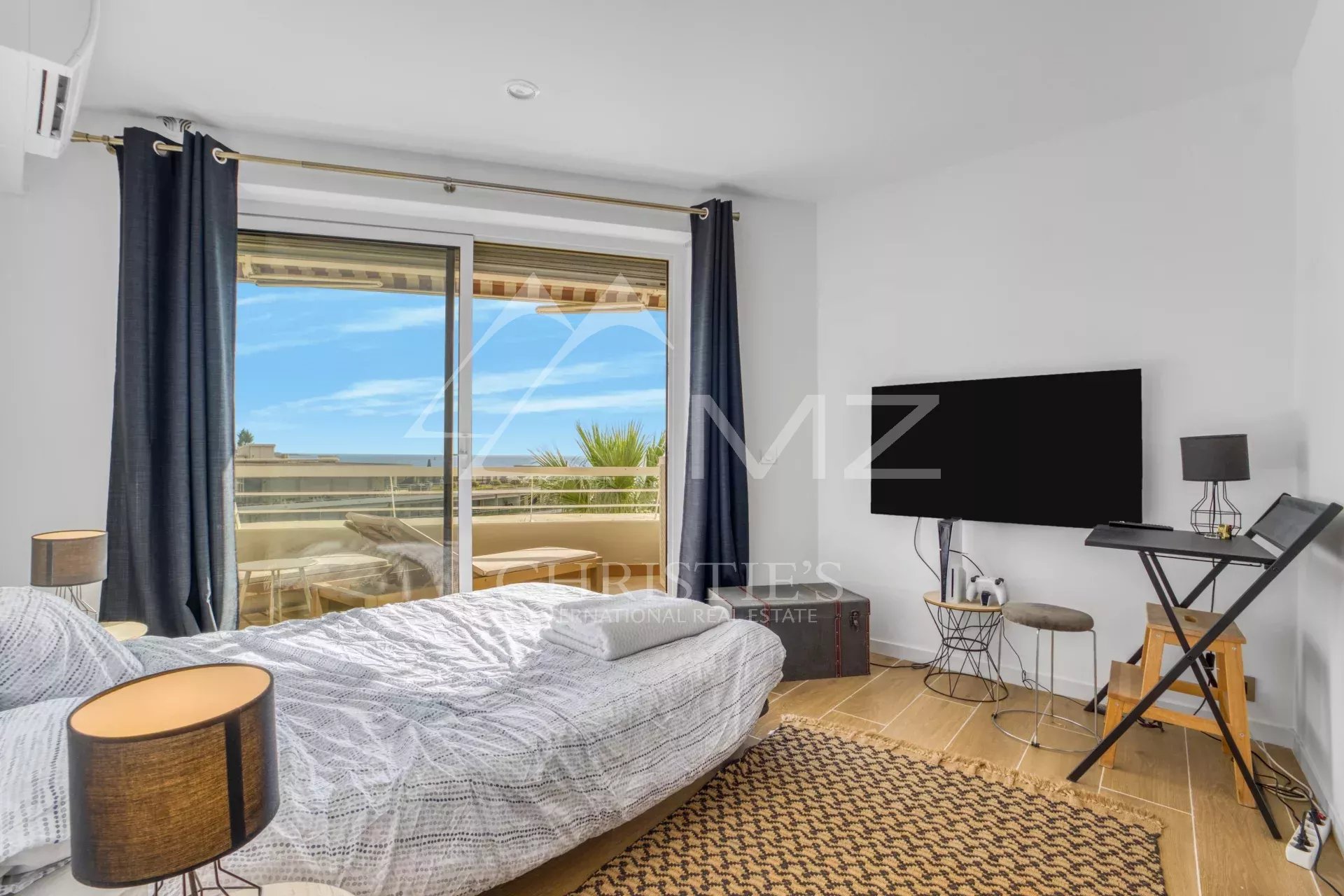 Chambre d'appartement avec vue sur la mer à Cannes, fenêtres ouvertes, décor moderne.
