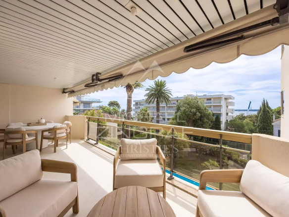 Apartment terrace in Cannes with garden furniture and views of the pool and palm trees.