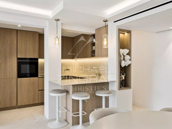 Modern open-plan kitchen with bar and high chairs in a renovated apartment in Cannes.